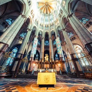 Intérieur d’une église en couleur, avec l’autel au premier plan, les colonnes et les vitraux sous une voûte lumineuse.