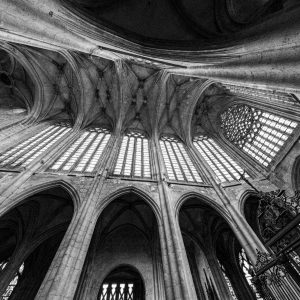 Colonnes et voûtes d’une église vues en contre-plongée oblique, en noir et blanc.