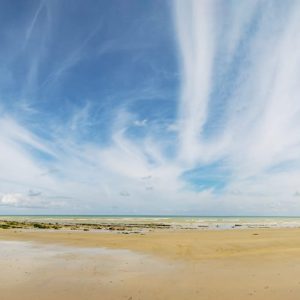 Panorama d’une plage ouverte sur la mer entre deux falaises, sous un ciel parcouru de nuages.