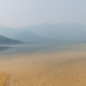 Panorama d’une étendue d’eau bordée d’une rive, avec des montagnes qui s’estompent dans la brume.