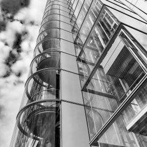 Vue en contre-plongée d'une cage d'escalier vitrée et des lignes verticales d'un bâtiment moderne se détachant sur le ciel.