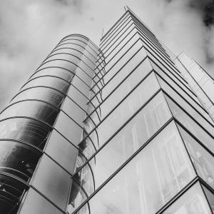 Tour vitrée arrondie et façade photographiées en contre-plongée, en noir et blanc.