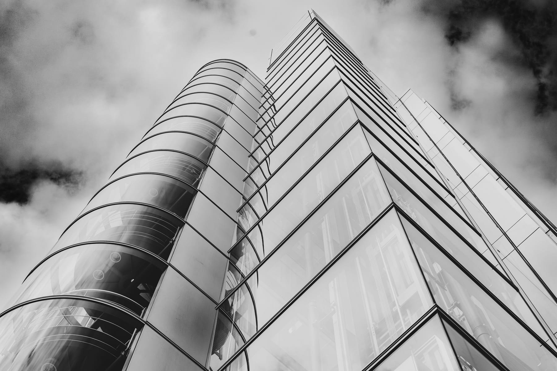 Tour vitrée arrondie et façade photographiées en contre-plongée, en noir et blanc.
