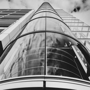 Paroi vitrée centrale et étages d’un bâtiment vus en contre-plongée, en noir et blanc.