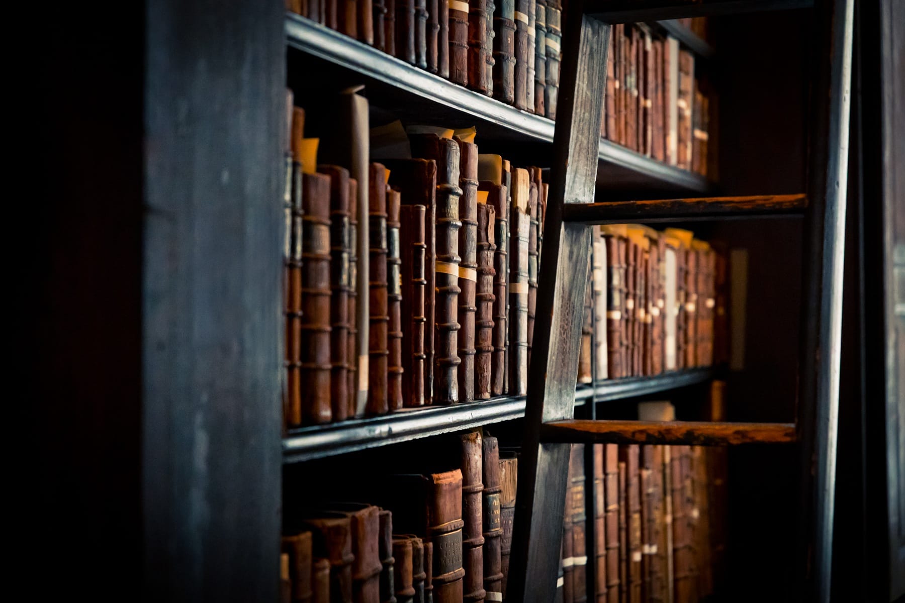 Livres anciens sur les étagères d’une bibliothèque, aux reliures éclairées par une lumière latérale.