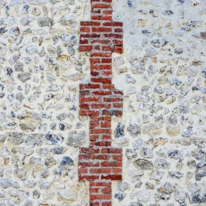 Mur de pierres claires traversé par une bande verticale de briques rouges.