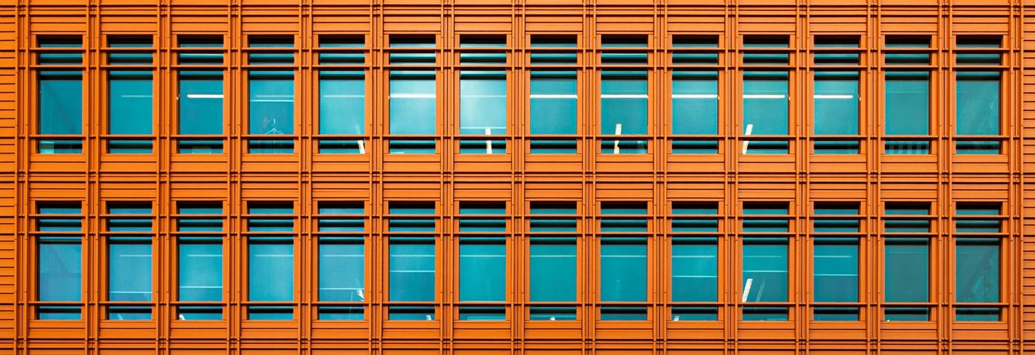 Façade orangée composée de rangées régulières de fenêtres bleutées, dans un cadrage horizontal allongé.