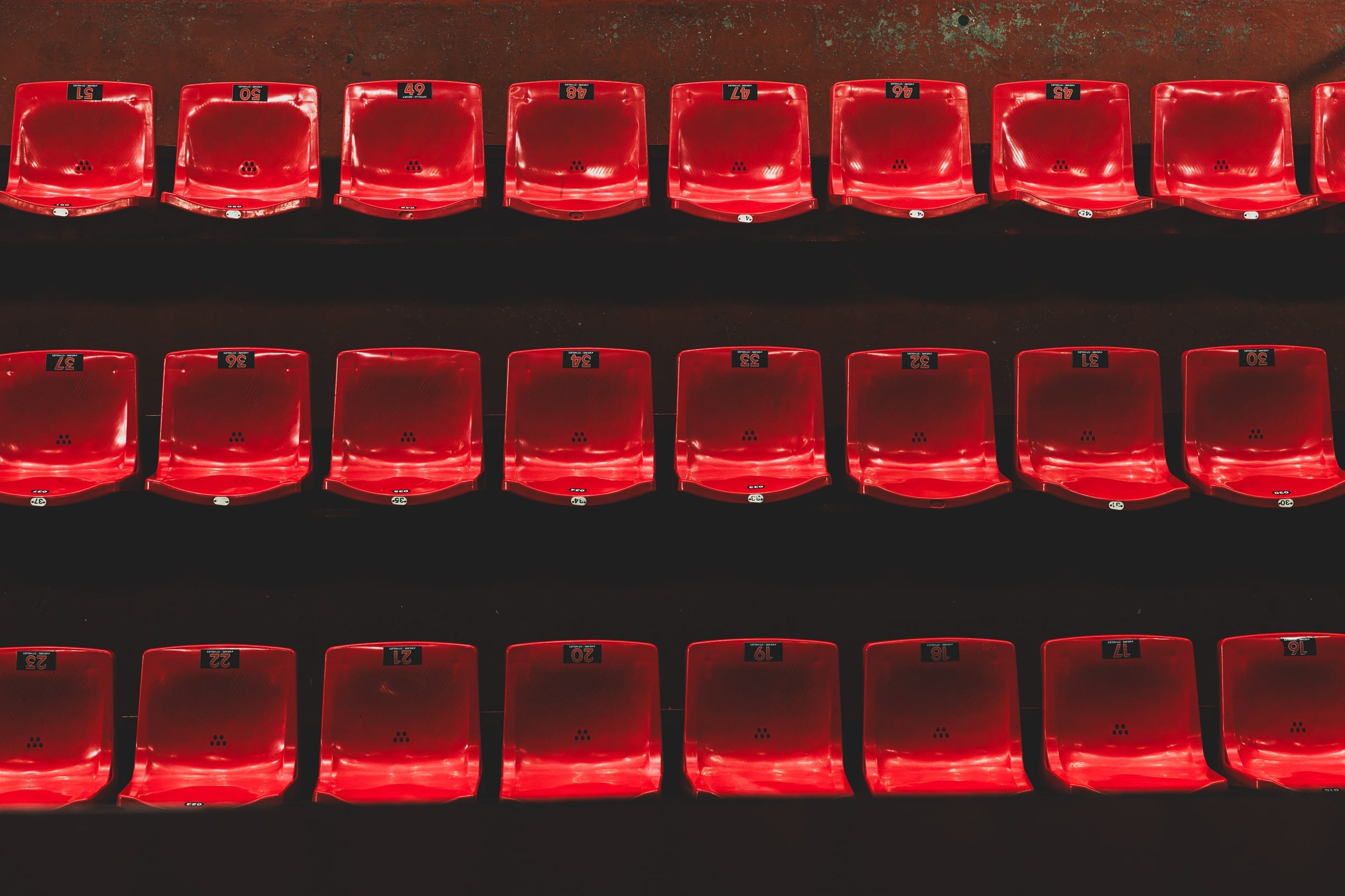 Rangées de sièges rouges formant des alignements réguliers sur un fond sombre.