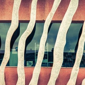 Éléments de façade ondulés se répétant devant des fenêtres, dans un cadrage horizontal.